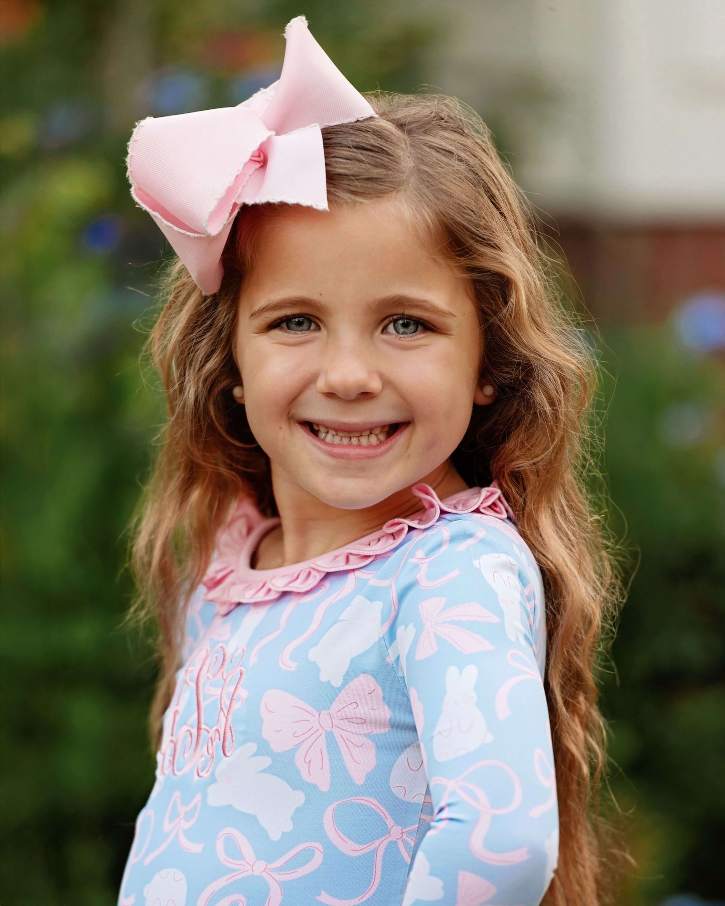 Young girl with a large pink bow in her hair, wearing a blue outfit with pink bows.