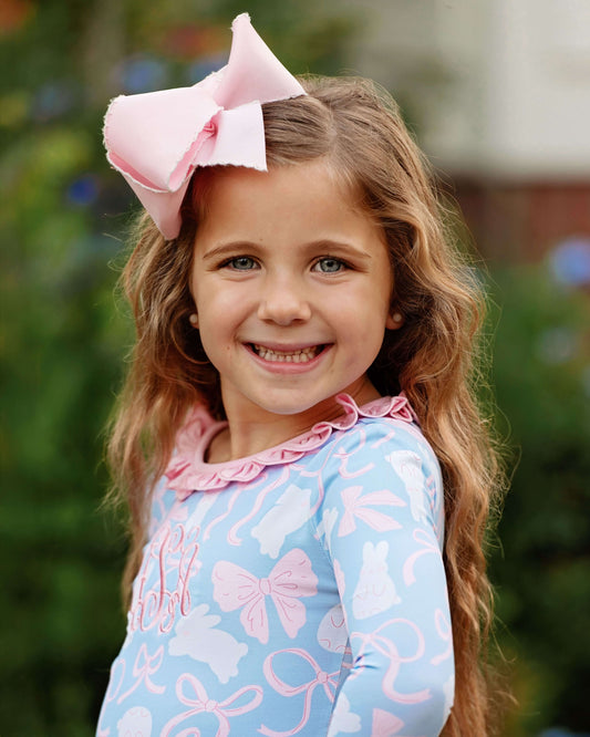 Young girl with a large pink bow in her hair, wearing a blue outfit with pink bows.