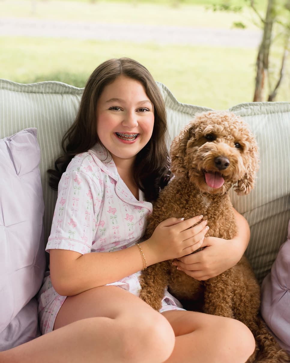 Young girl with braces holding a brown dog on a couch outdoors
