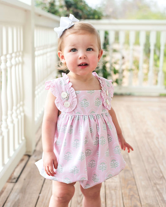 baby girl wearing a pink floral bubble standing on a porch