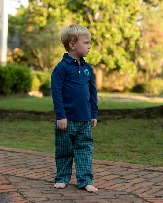 boy in a green and navy pants set standing on a brick path with greenery in the background