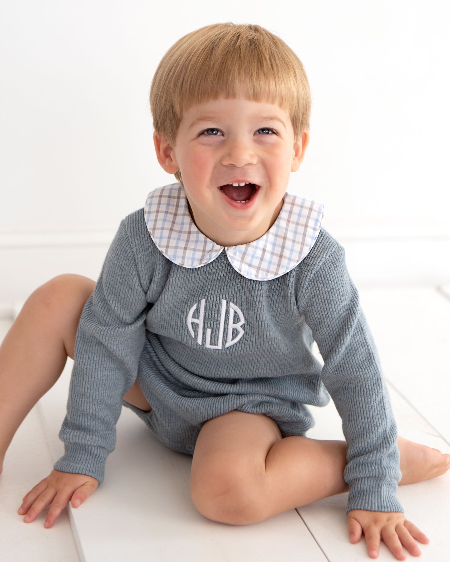 boy wearing a gray bubble with a checkered collar and monogram on a white background