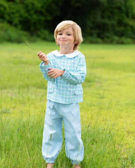 Child in a checkered shirt and light blue pants standing in a grassy field