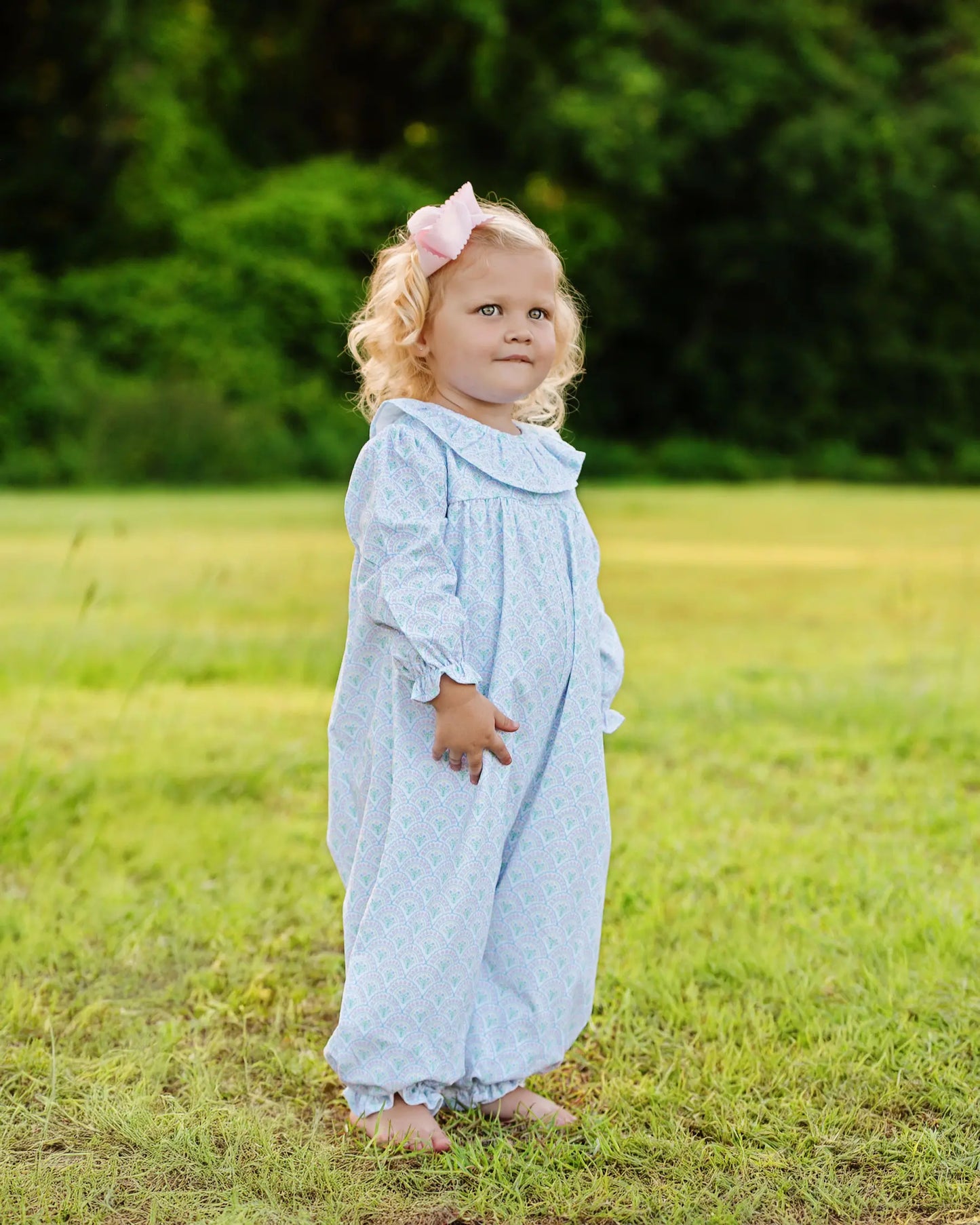 Child in a light blue dress standing in a grassy field with a blurred green background