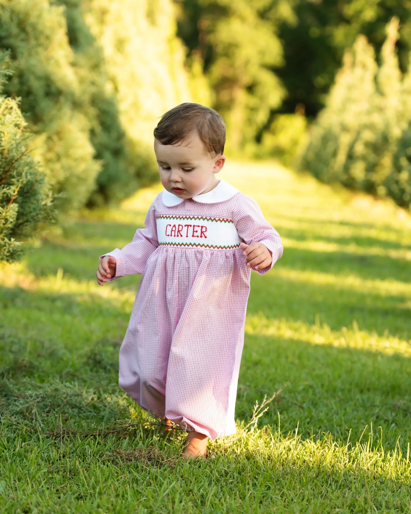 Child in a red outfit with 'Carter' text standing in a grassy area with trees in the background