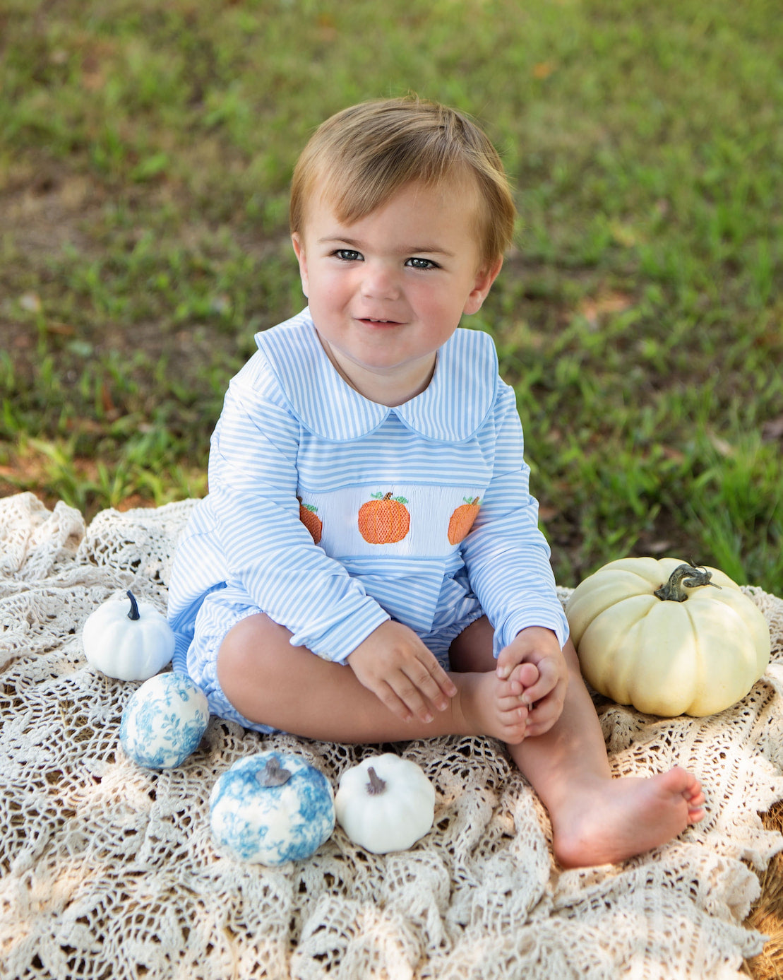 Child sitting on a lace blanket with pumpkins in an outdoor setting
