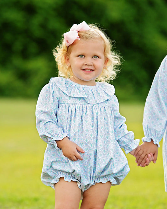 Child wearing a light blue floral dress with a blurred green background
