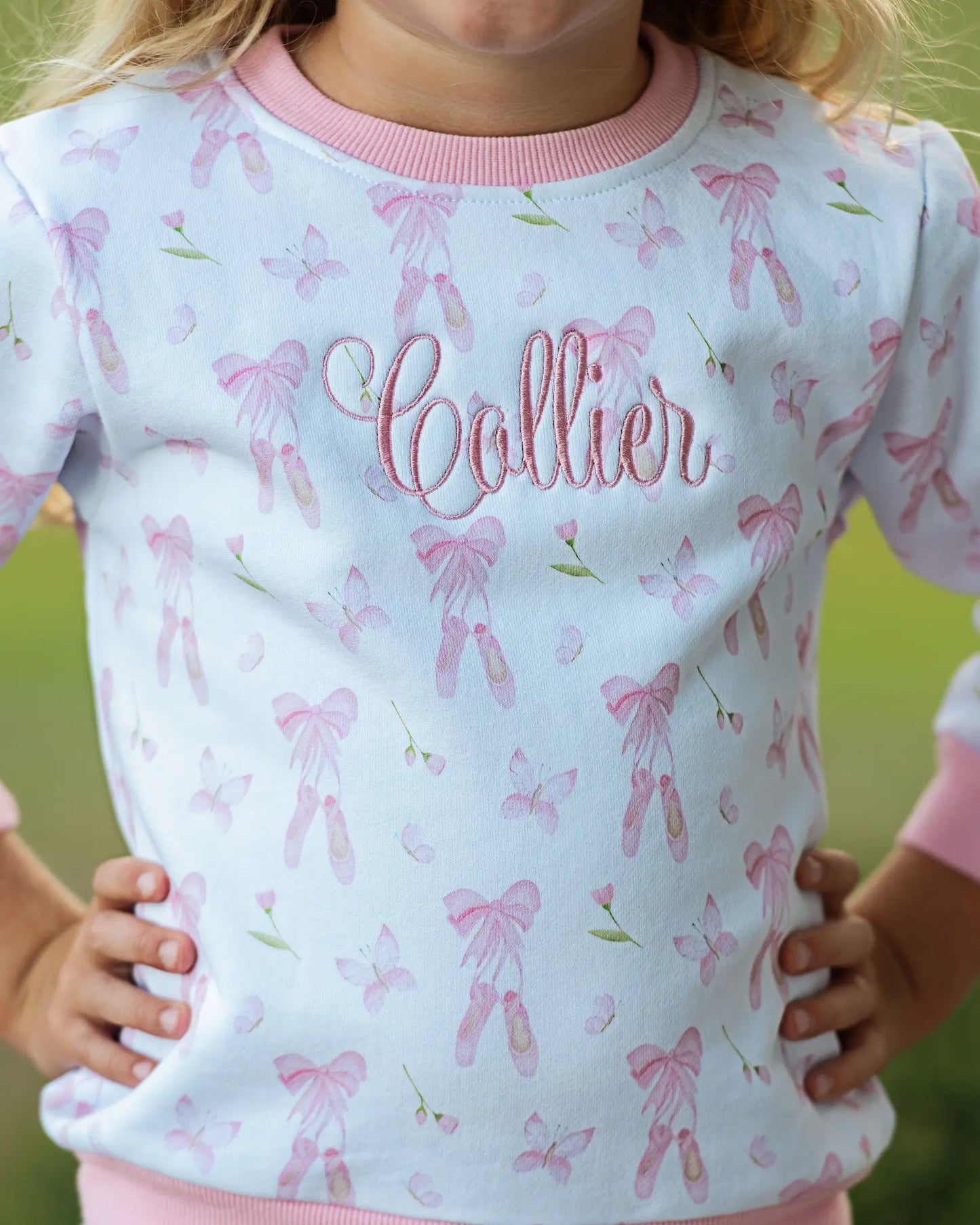 Child wearing a light blue shirt with pink bow pattern and 'Collier' text.