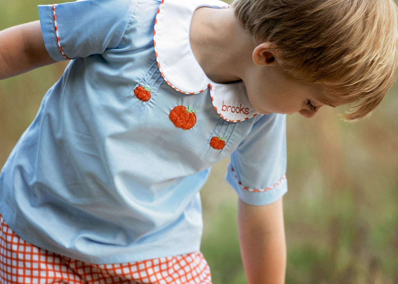 Child wearing a light blue shirt with red floral patterns and 'brooks' branding, standing outdoors.