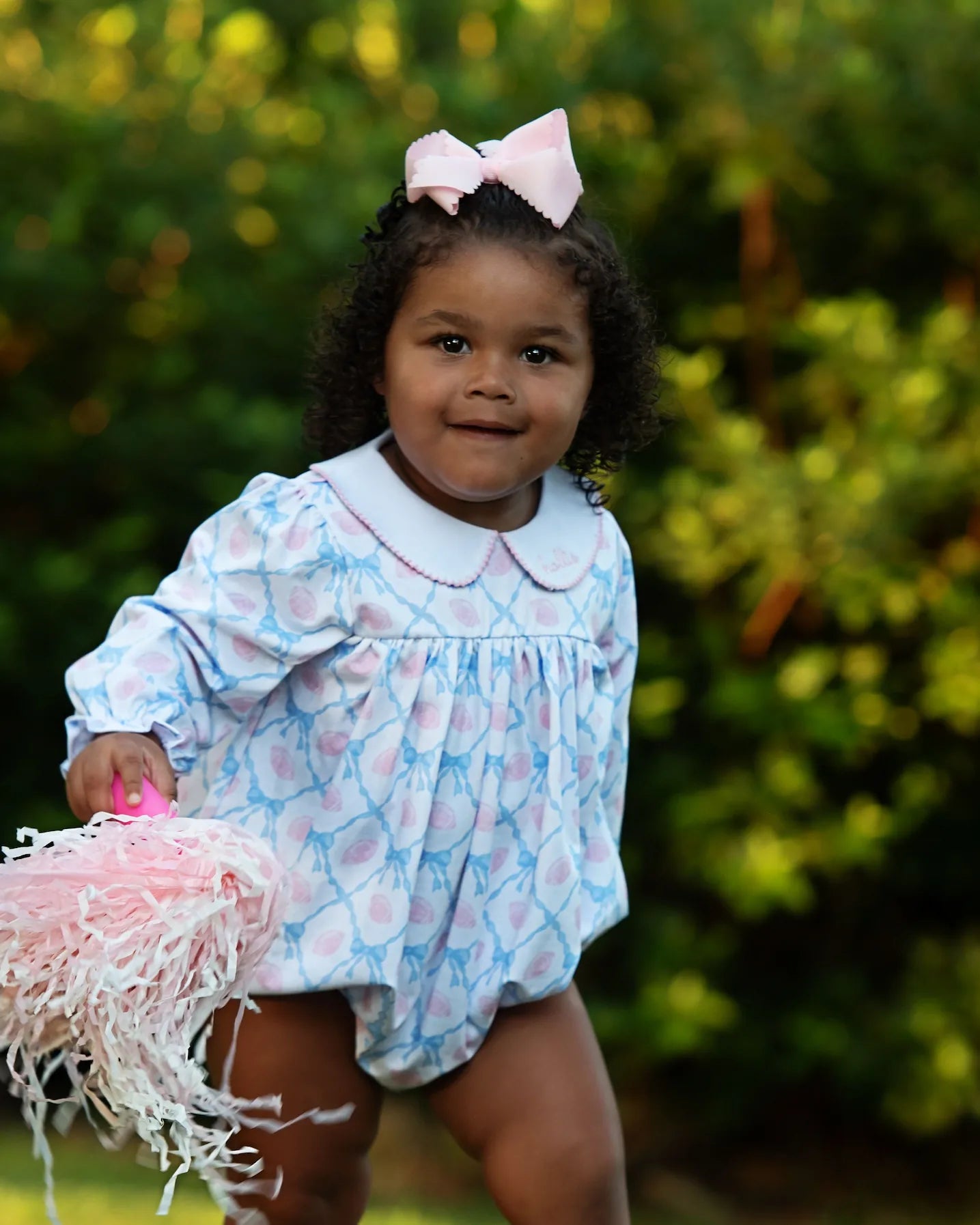 Child wearing a patterned dress with a pink bow outdoors