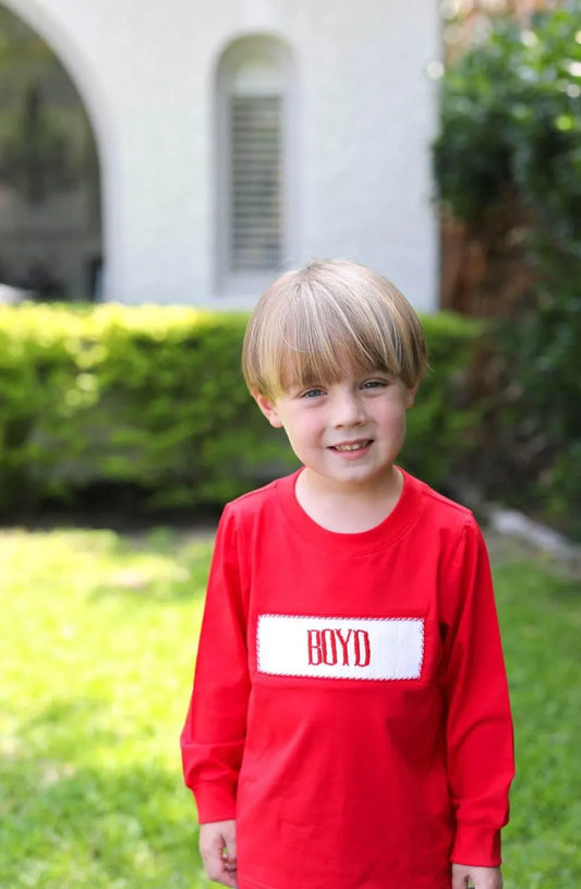 Child wearing a red shirt with 'BOYD' on it, standing outdoors.