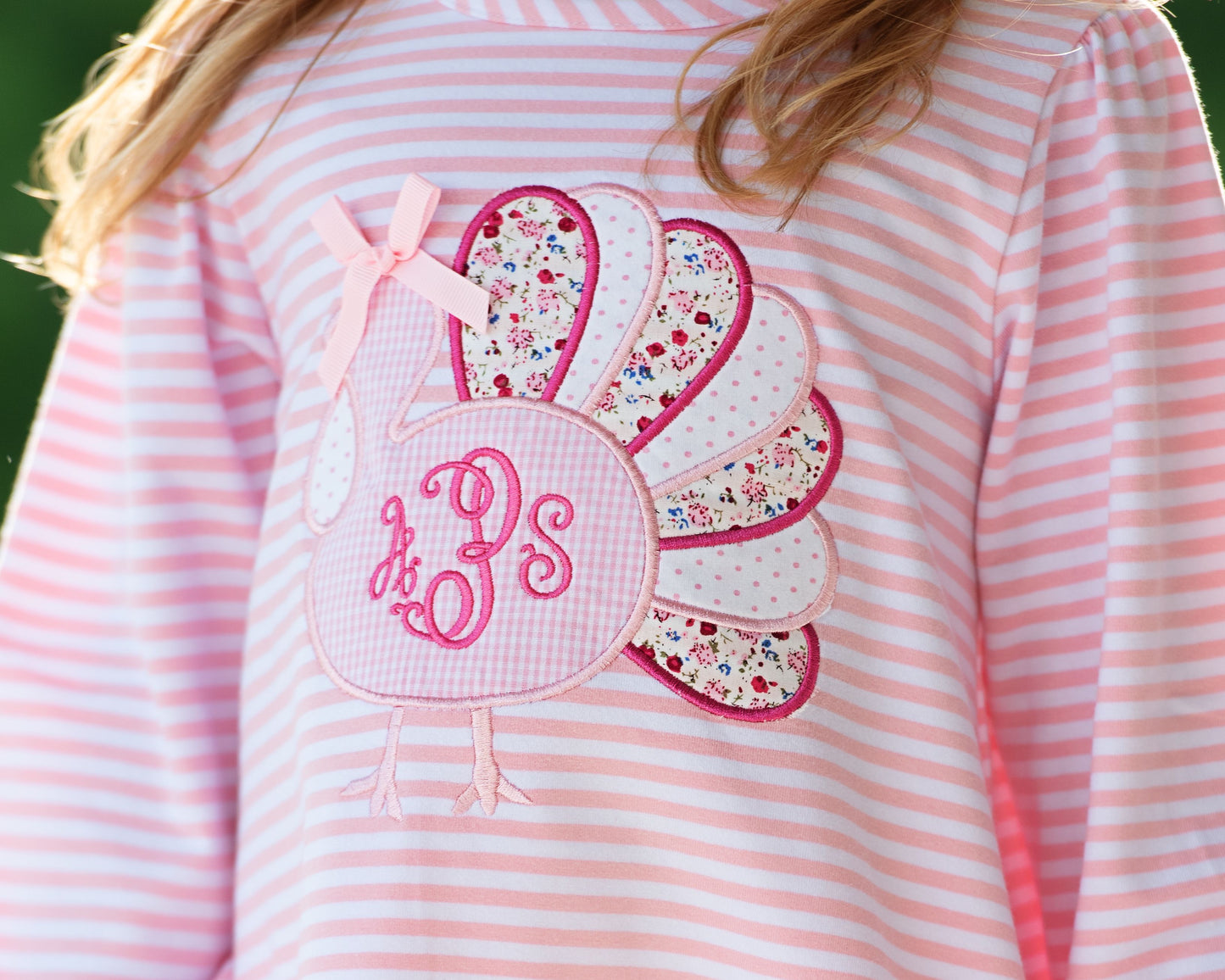 close up of pink and white striped legging set with floral turkey and monogram "aPs' on a blurred green background
