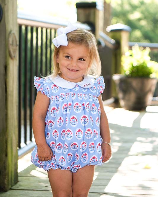girl in floral blue outfit with white bow standing on a porch