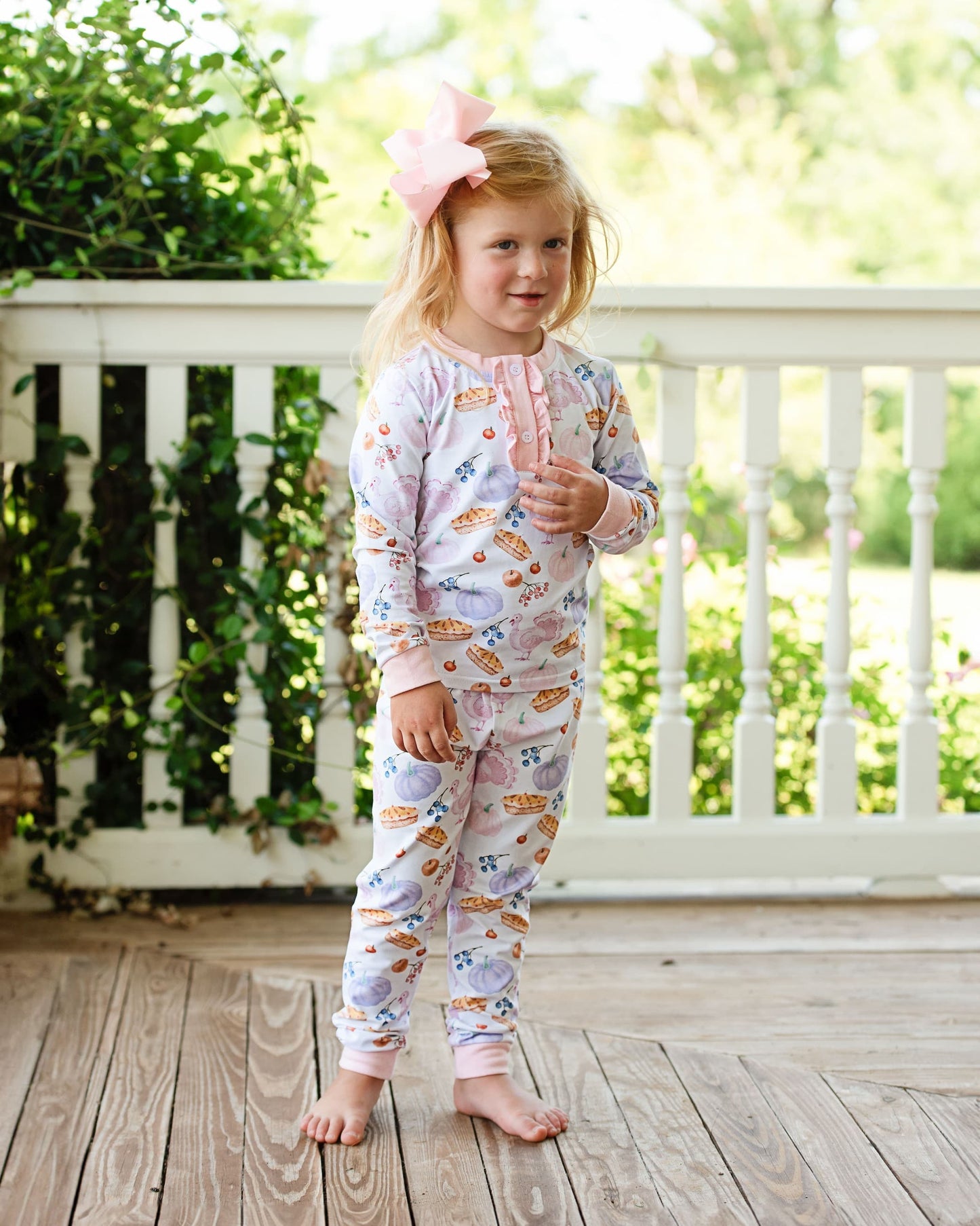 girl in pajamas standing on a wooden deck with greenery in the background