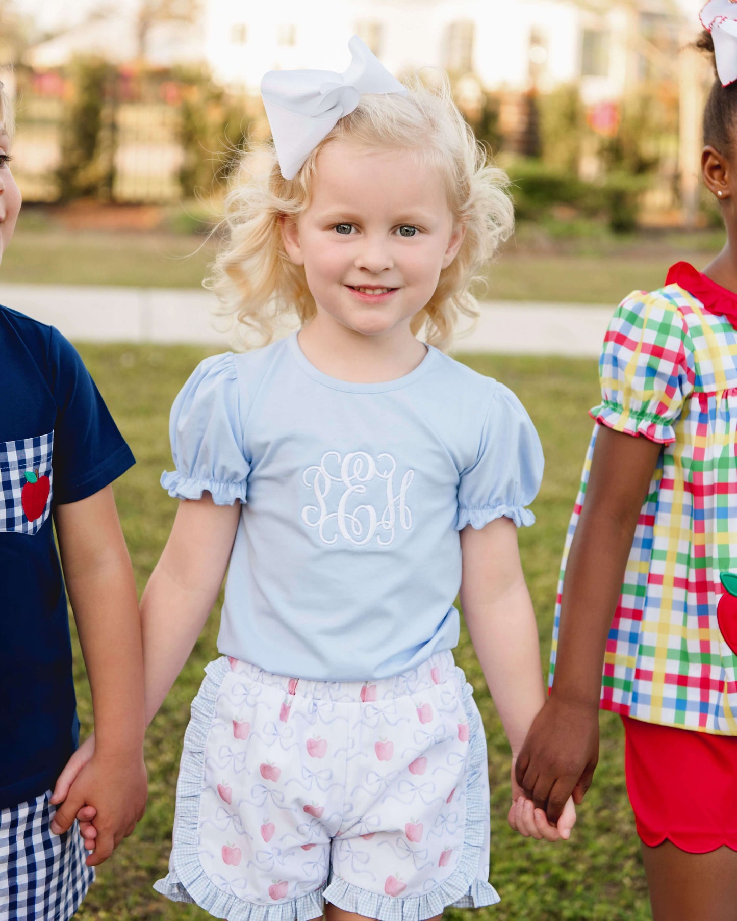 girl wearing blue shirt and apple print shorts standing outdoors.