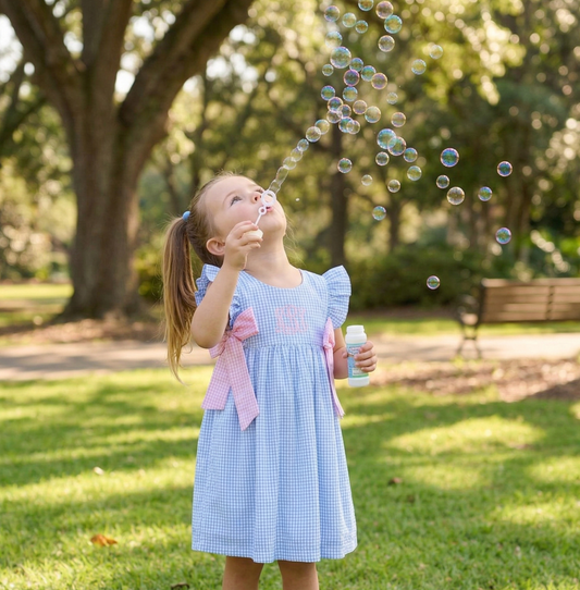 little girl searing a blue gingham dress blowing bubbles