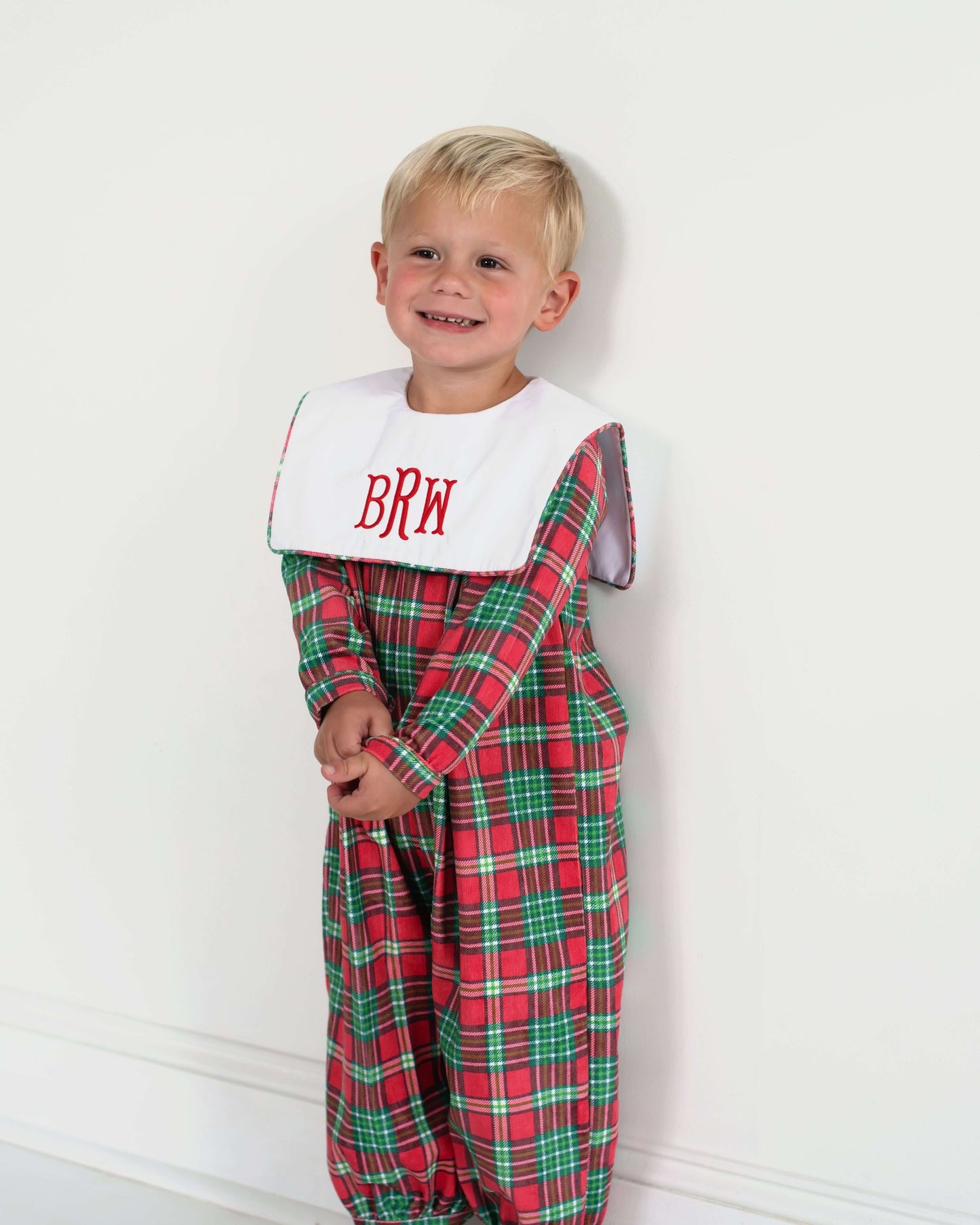 Child wearing a red plaid outfit with a white bib against a white background