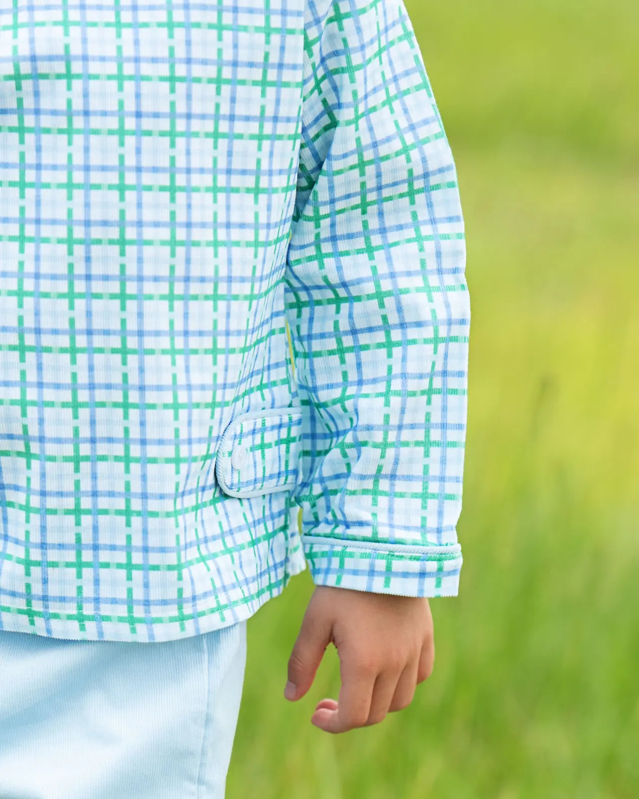 Person wearing a green and white checkered shirt in a grassy field