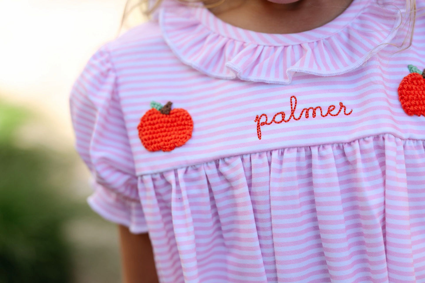 Pink and white striped dress with embroidered pumpkins and 'palmer' text on a blurred background