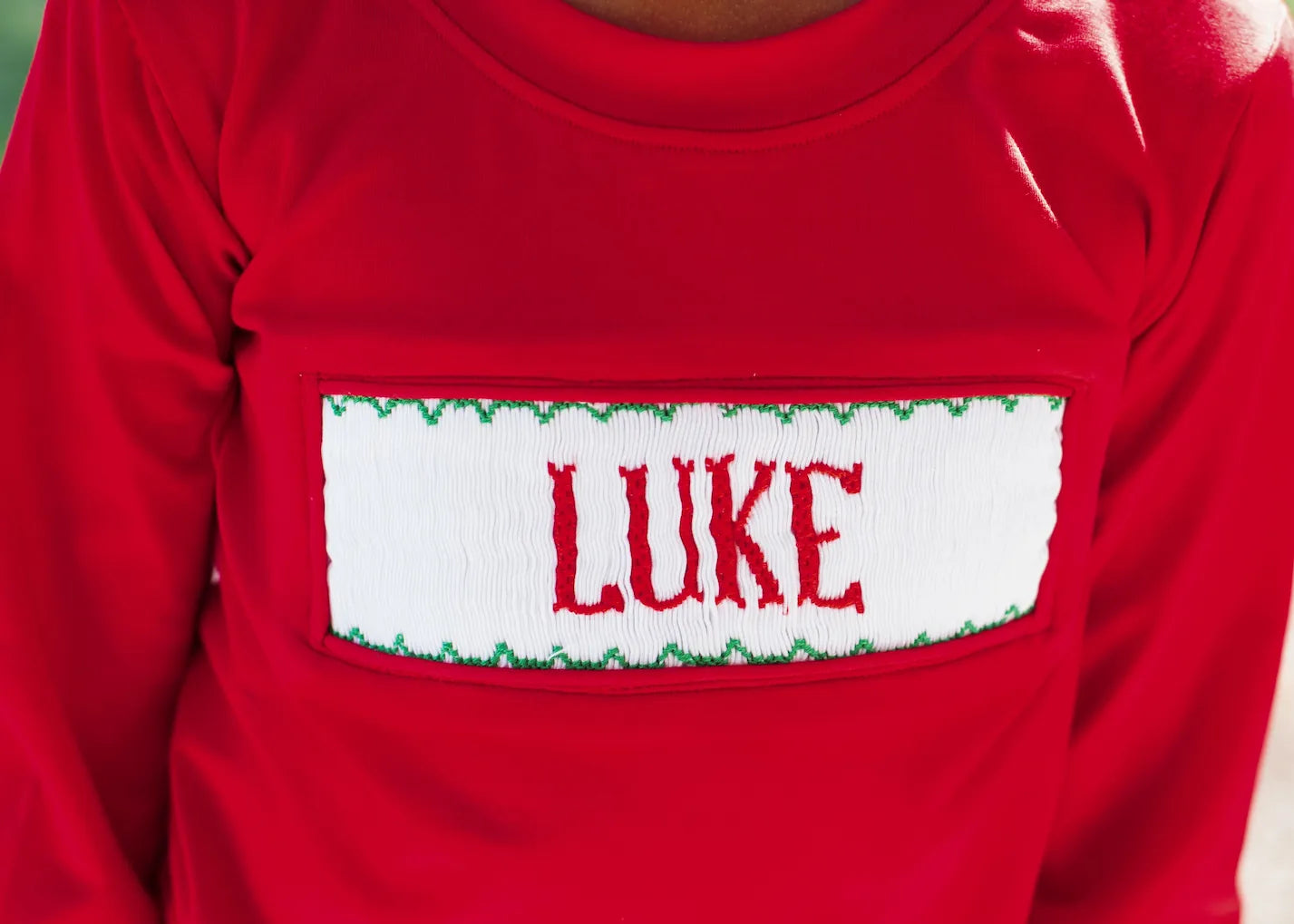 Red shirt with a name patch displaying 'LUKE' on a plain background