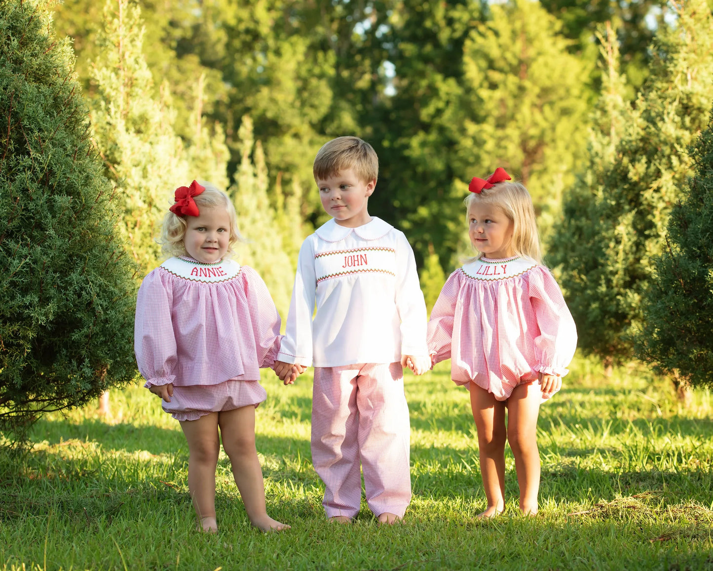 Three children in matching outfits standing in a grassy area with trees in the background