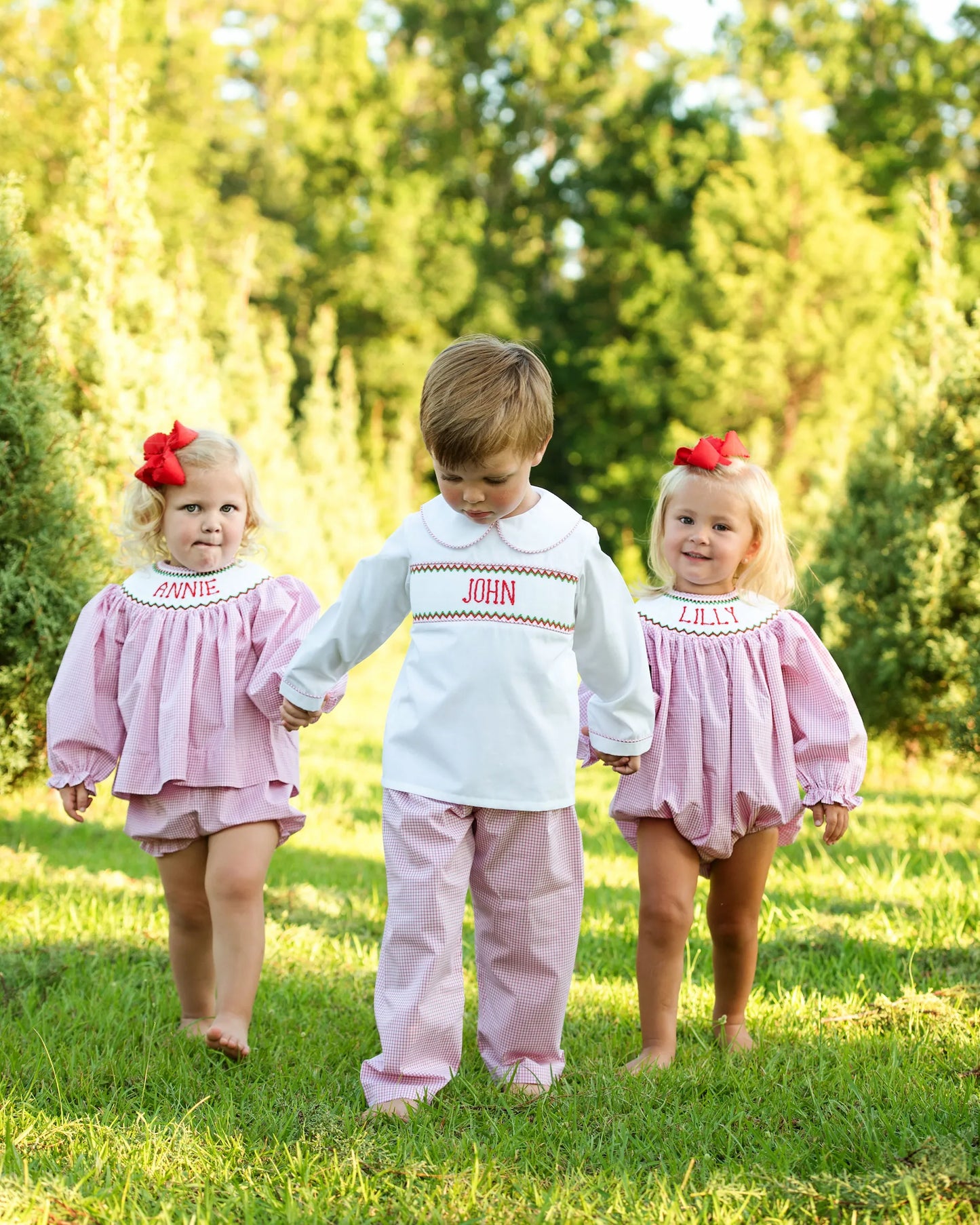 Three children in matching outfits with embroidered names walking outdoors.