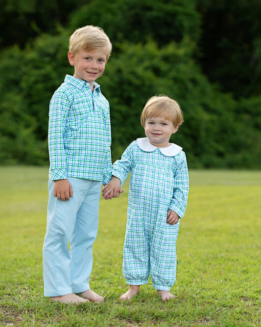 Two children in matching blue checkered outfits standing on grass with a blurred green background