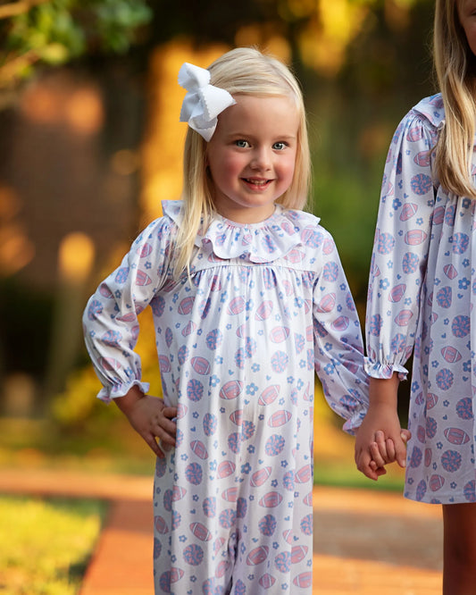Two children in matching floral dresses standing outdoors with a blurred natural background