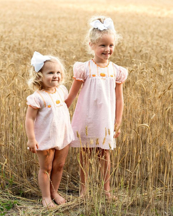 two young girls in matching dresses standing in a field of tall grass