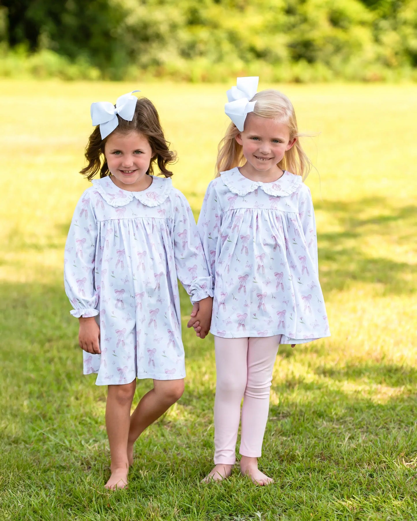 Two young girls in matching dresses standing in a grassy field.