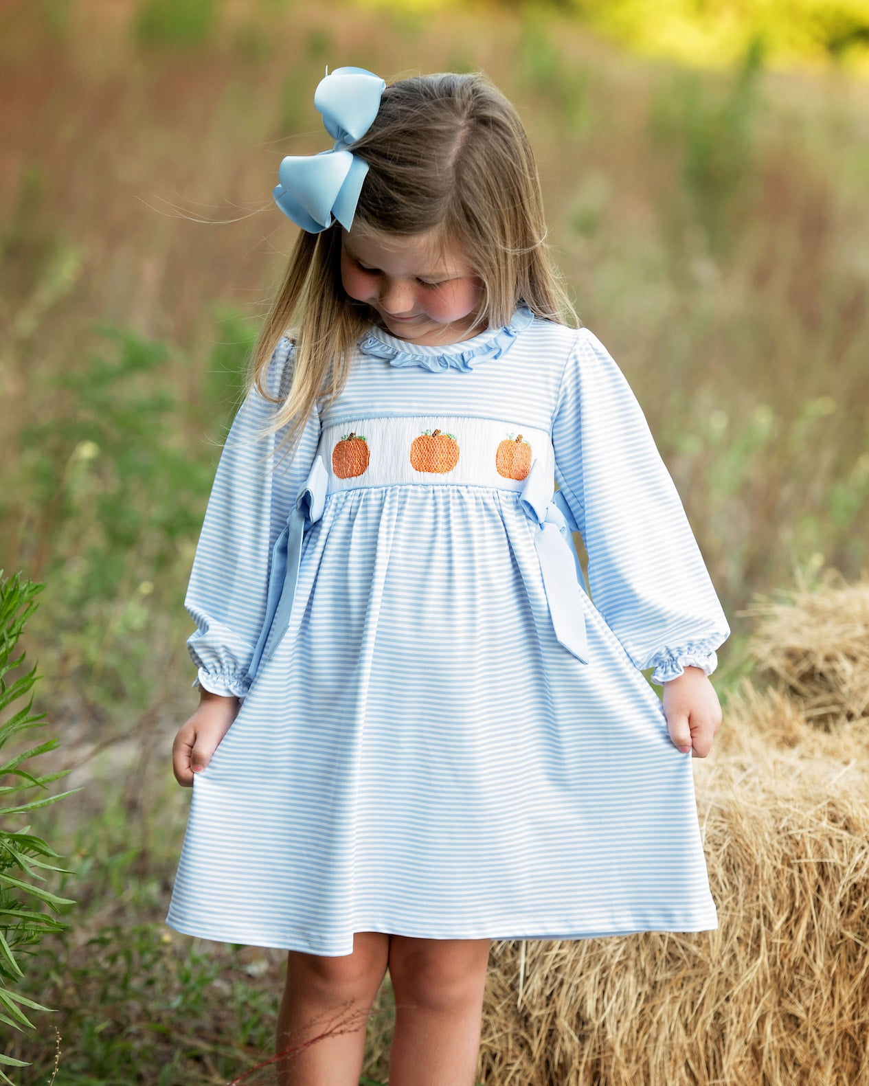 Young girl in a blue dress with pumpkin designs standing in a field.
