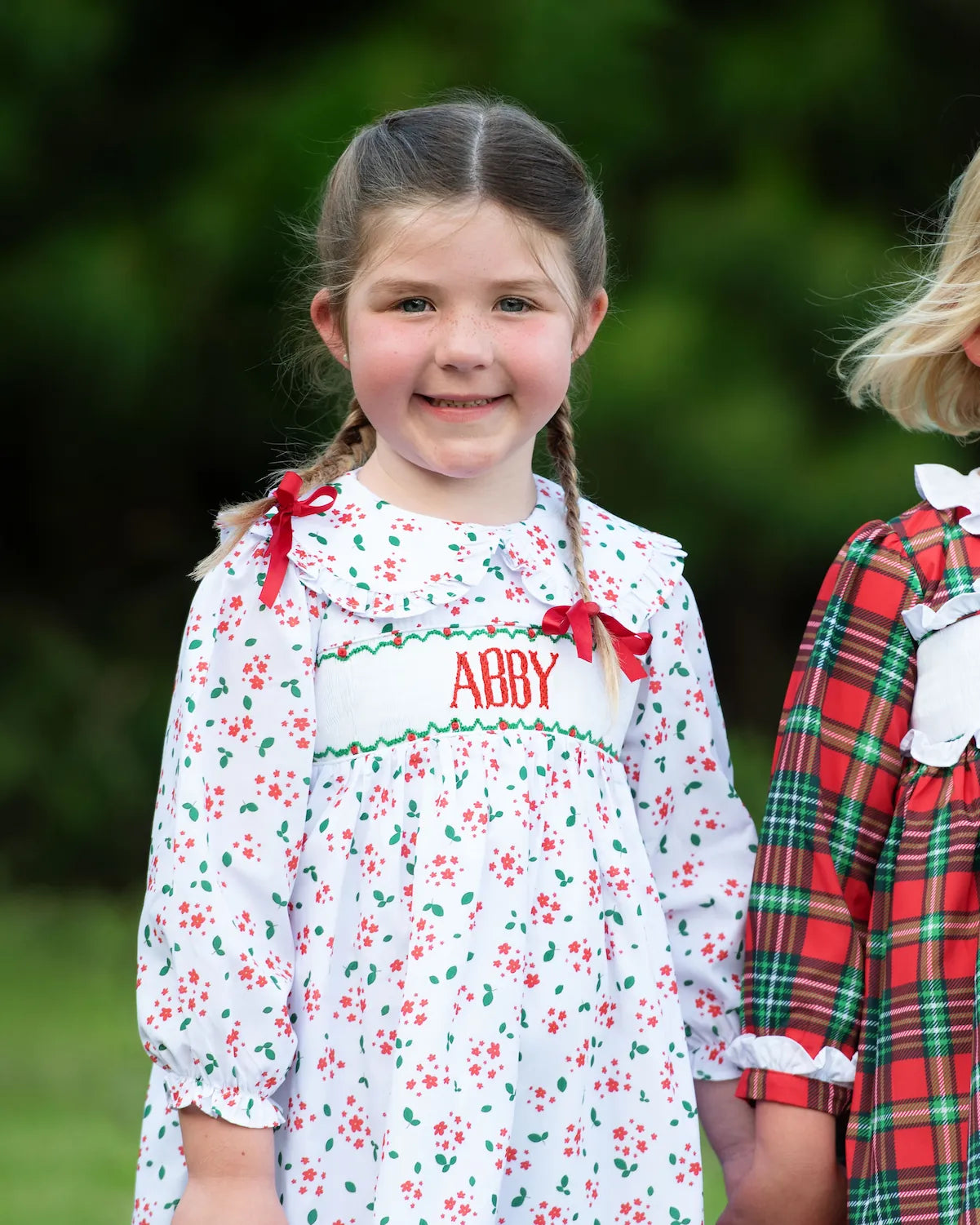 Young girl wearing a floral dress with 'ABBY' embroidered on it, standing outdoors.