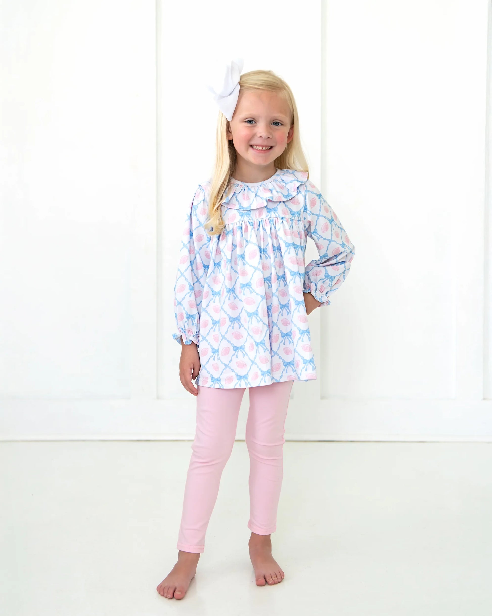 Young girl wearing a patterned top and pink pants on a white background