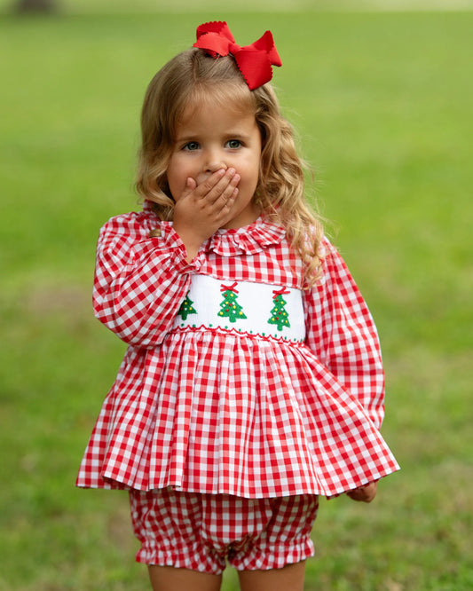 Young girl wearing a red and white checkered outfit with a red bow in her hair, standing on grass.