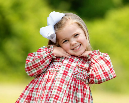 Young girl wearing a red plaid dress with a large white bow outdoors