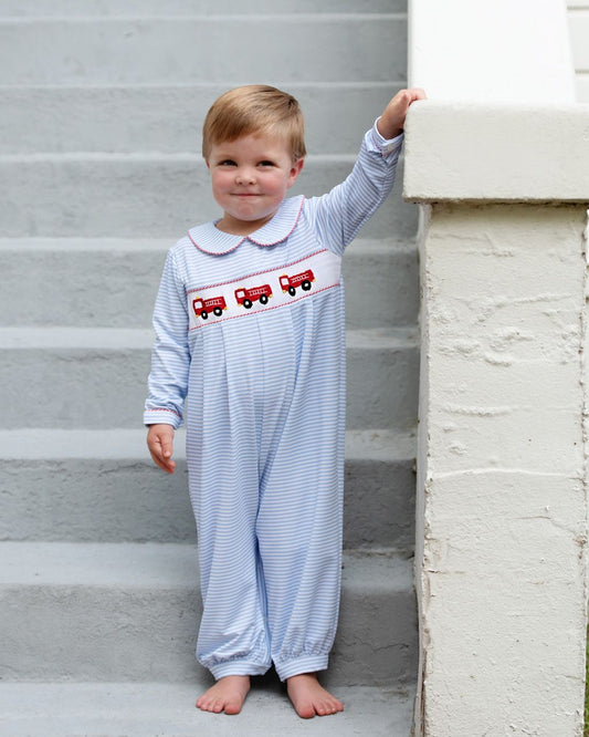 young boy wearing a blue striped long romper with fire truck design on a staircase