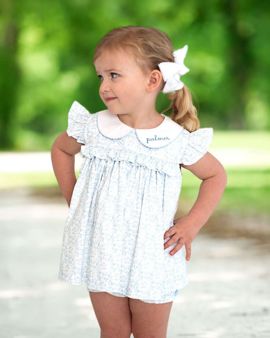 young girl posing in a blue and white floral diaper set standing outside