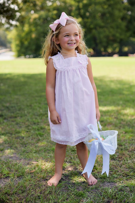 Girl wearing pink embroidered dress outdoors holding Easter basket, full length view