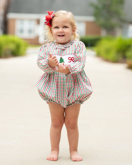young girl standing outside wearing a red and green bubble with a smocked Christmas tree and bow