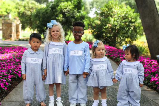 Five children wearing personalized light blue custom smocked outfits with name panels outdoors