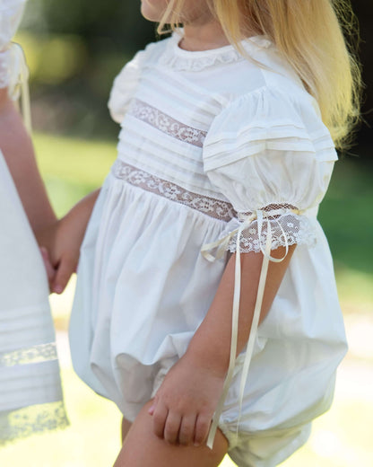 Child wearing a white dress with lace details in an outdoor setting