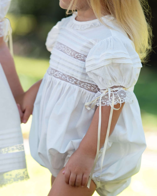 Child wearing a white dress with lace details in an outdoor setting