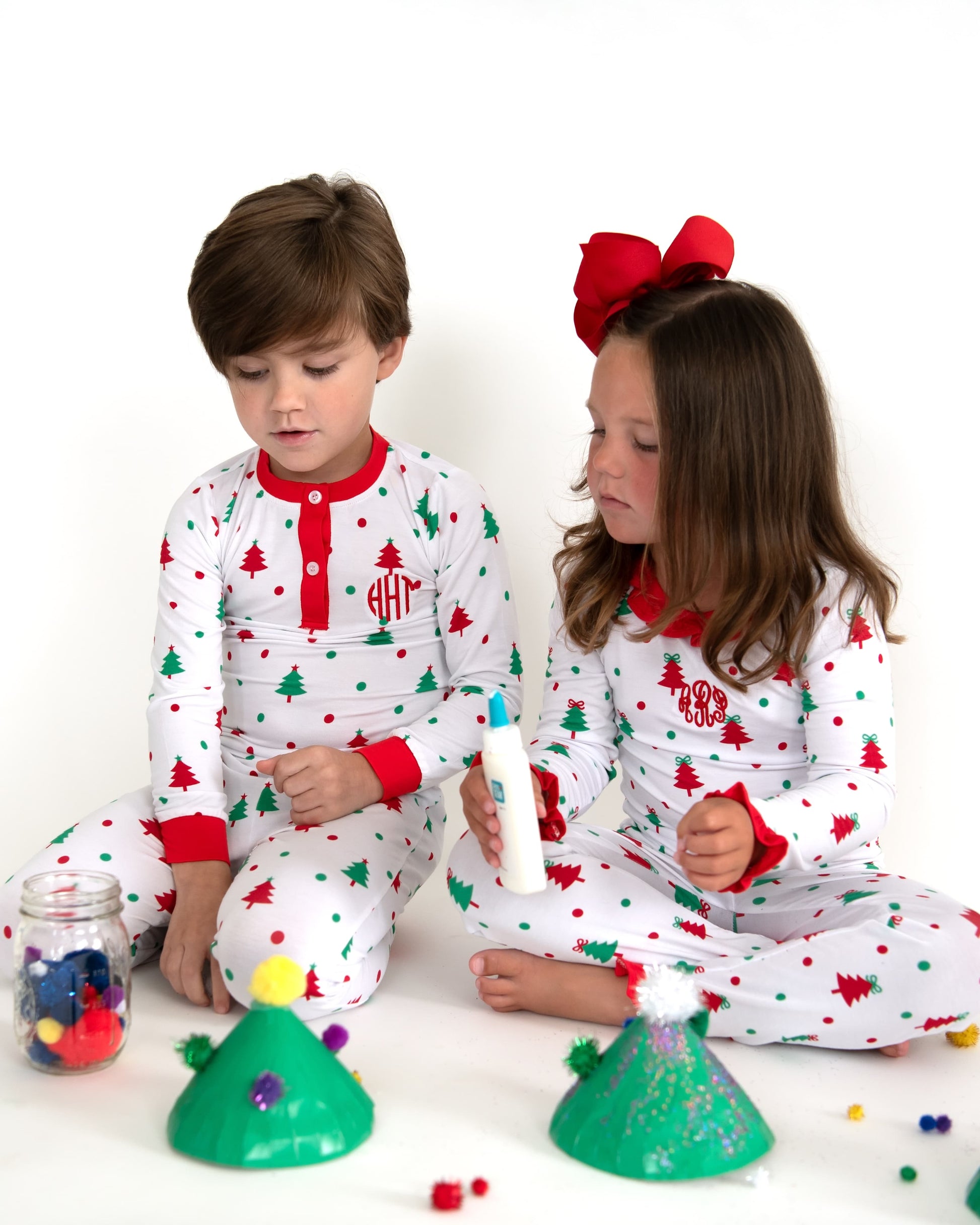 A boy and a girl in matching Christmas pajamas making crafts.
