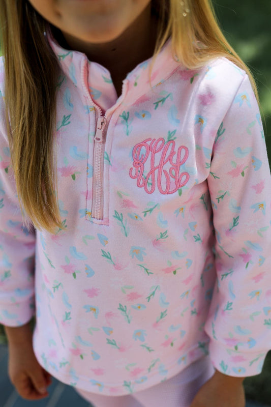 A close up of a young girl wearing a pink and blue floral fleece pullover with a half zipper