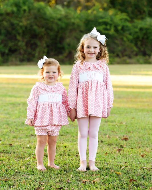 A couple of young girls in matching pink heart outfits standing on grass with a blurred background