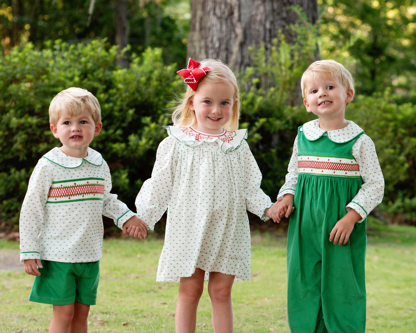 A girl and two boys standing outdoors on grass, wearing matching coordinated outfits. 