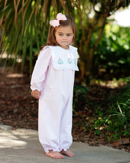 A little girl standing outside wearing a pink striped knit long bubble with a white square collar, featuring three embroidered Christmas trees