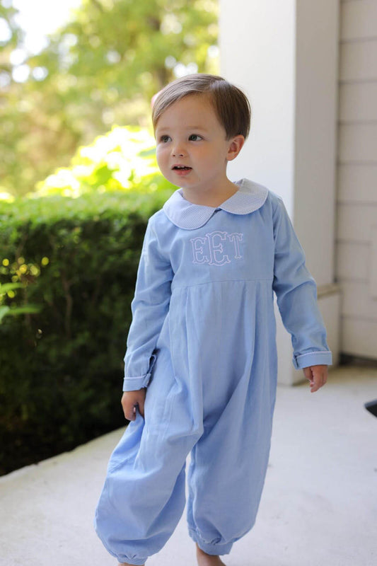 A toddler standing outdoors on a porch wearing a light blue long-sleeve footless jumpsuit with a white Peter Pan collar and the name 'ECT' embroidered on the chest.