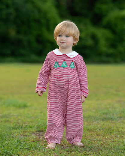 A toddler standing outdoors on grass wearing a pink and white striped footless one-piece jumpsuit with a white Peter Pan collar and three green embroidered trees on the chest.