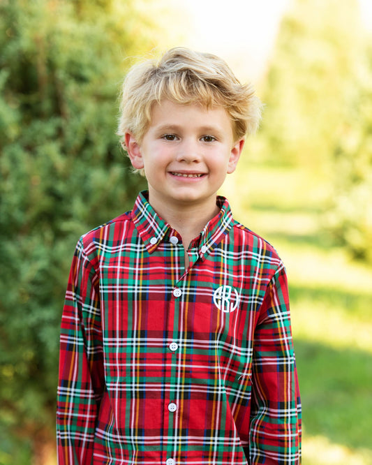A young blond boy smiling outdoors, wearing a red plaid button-down shirt with green, white, and yellow stripes and a white monogram logo on the chest.
